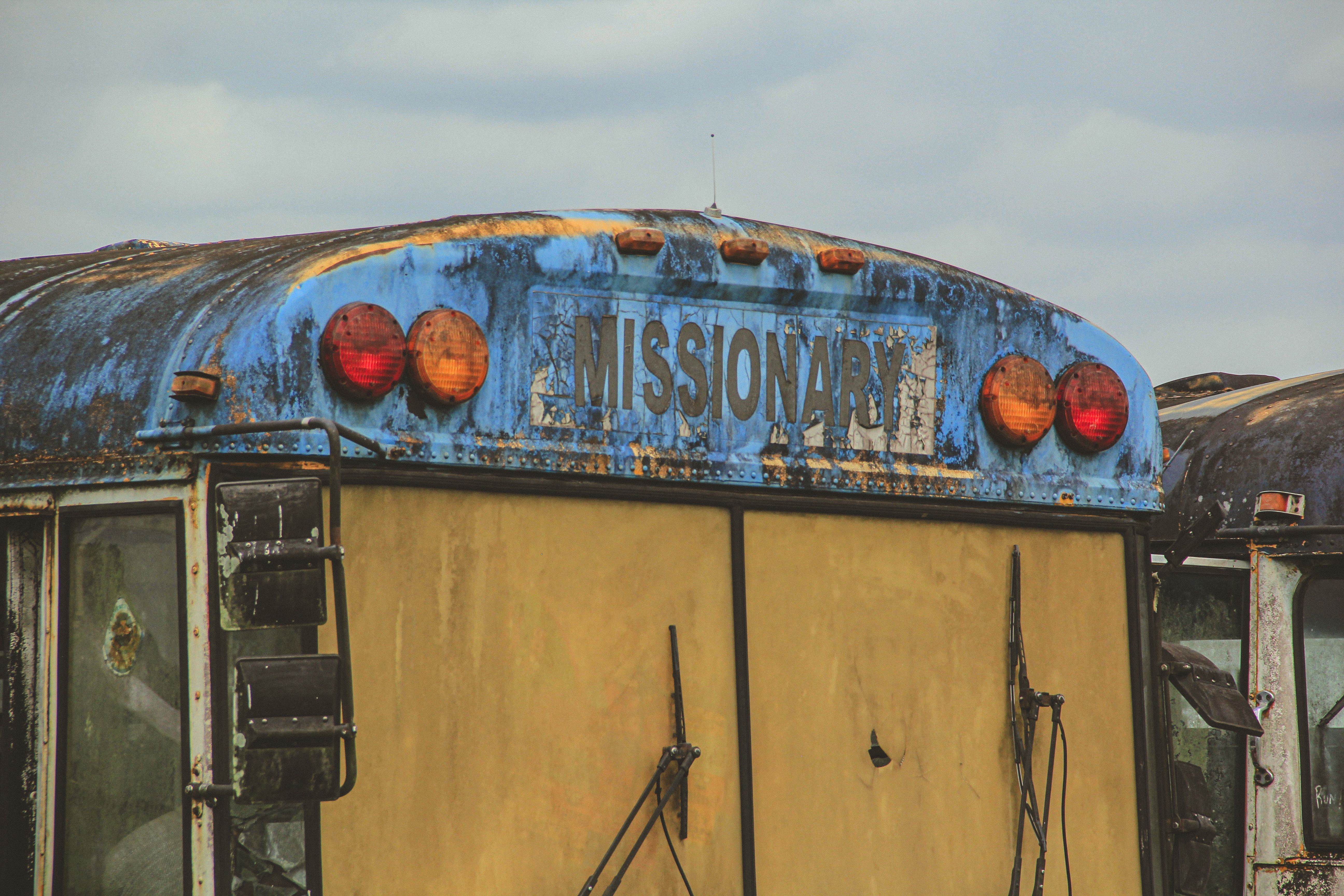 A decaying, weathered bus with 'Missionary' sign in a neglected outdoor setting.