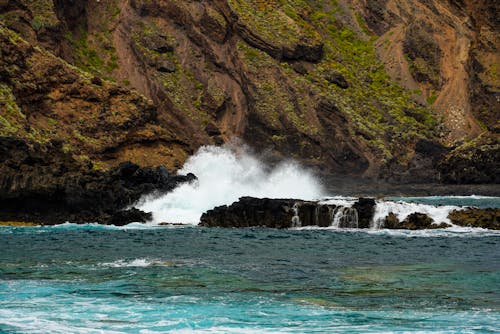 A large wave crashing into the rocks near the shore