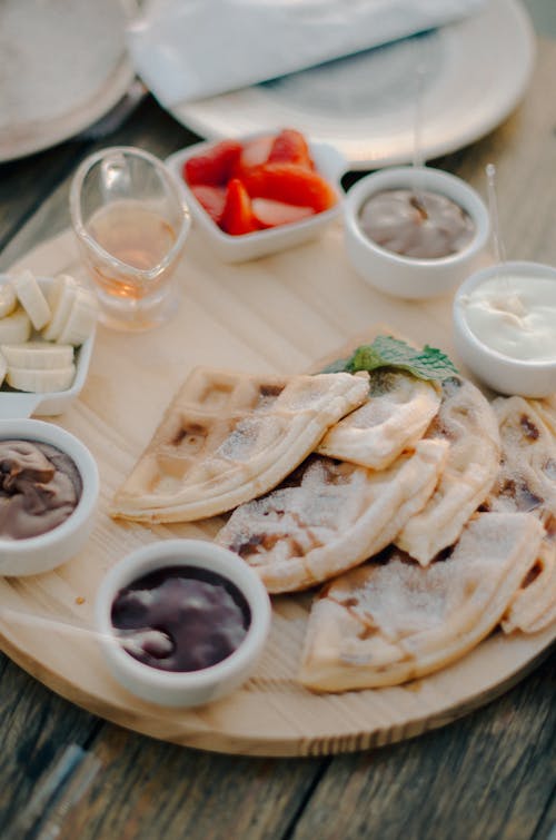 A wooden plate with waffles and dips on it