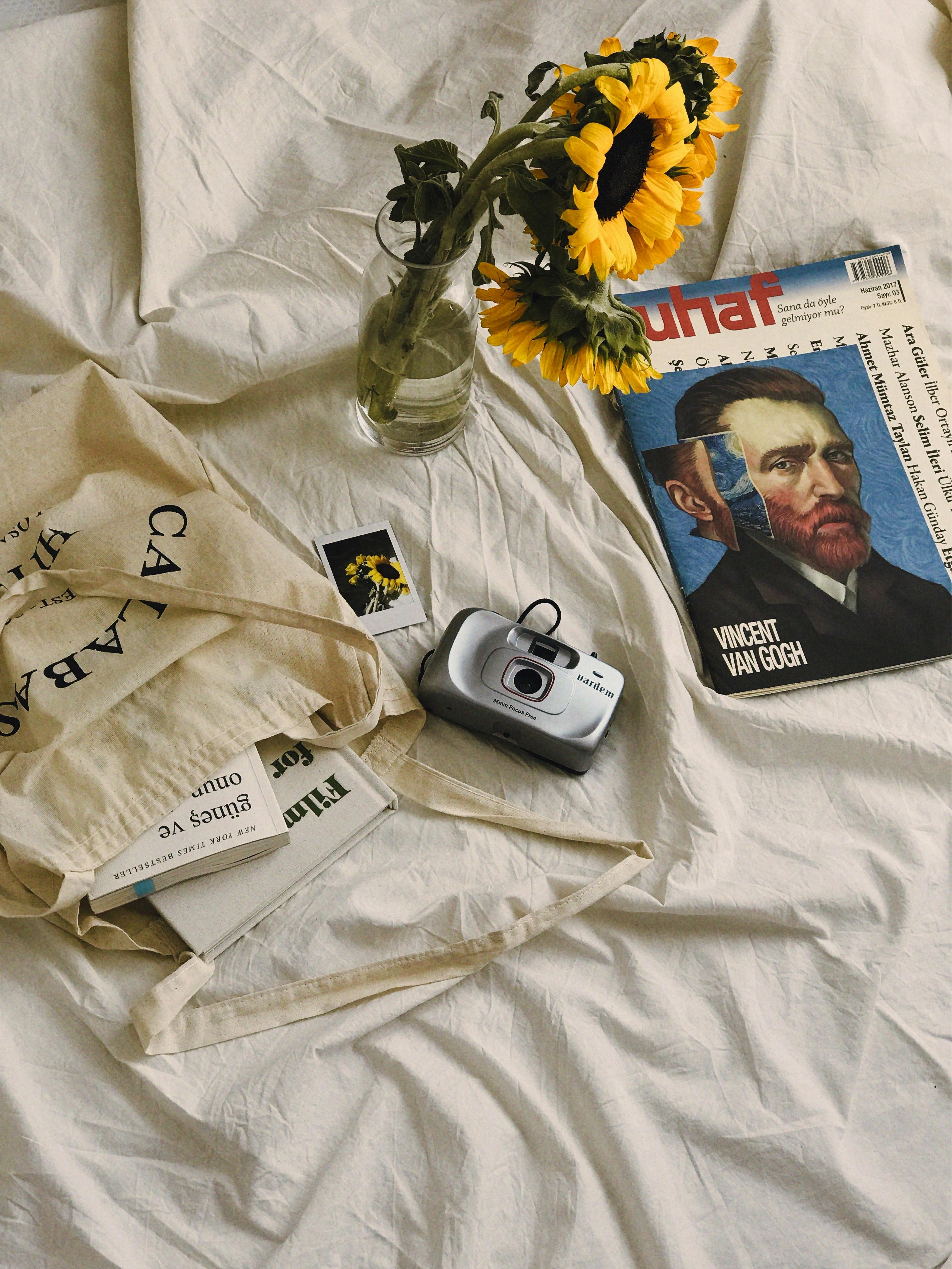 Elegant flat lay featuring a Van Gogh magazine, sunflowers, and a camera on beige fabric.