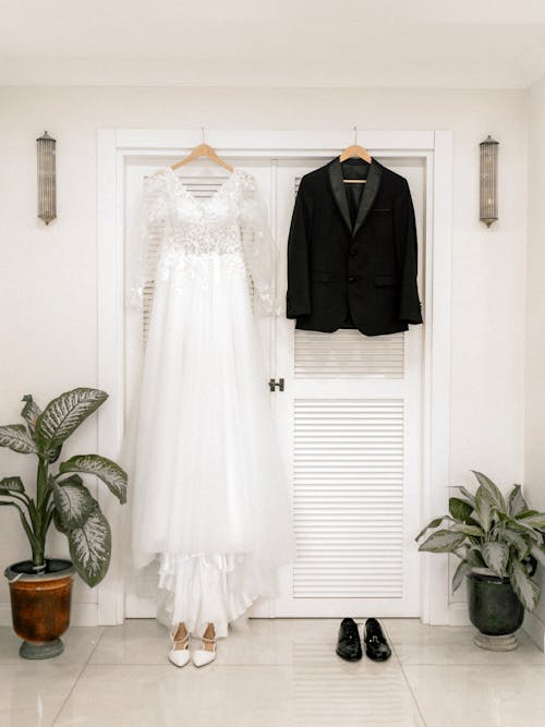 A wedding dress and suit hanging on a door