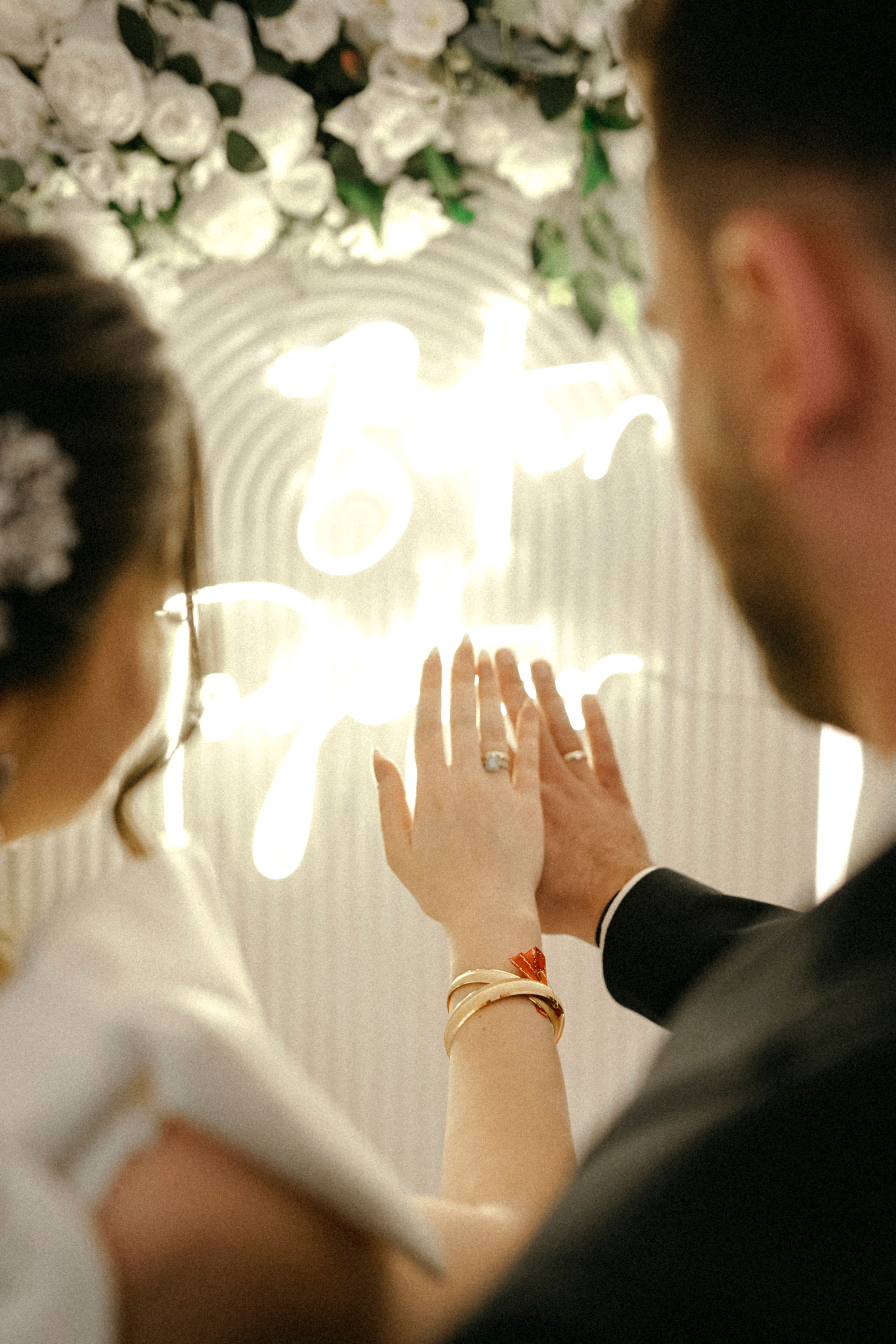 Bride and groom showcase wedding rings with floral decoration backdrop.