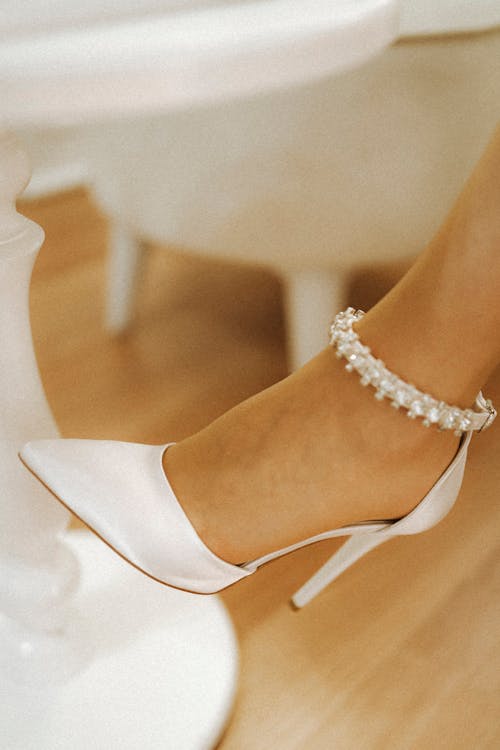 A woman's feet are wearing white shoes with pearls
