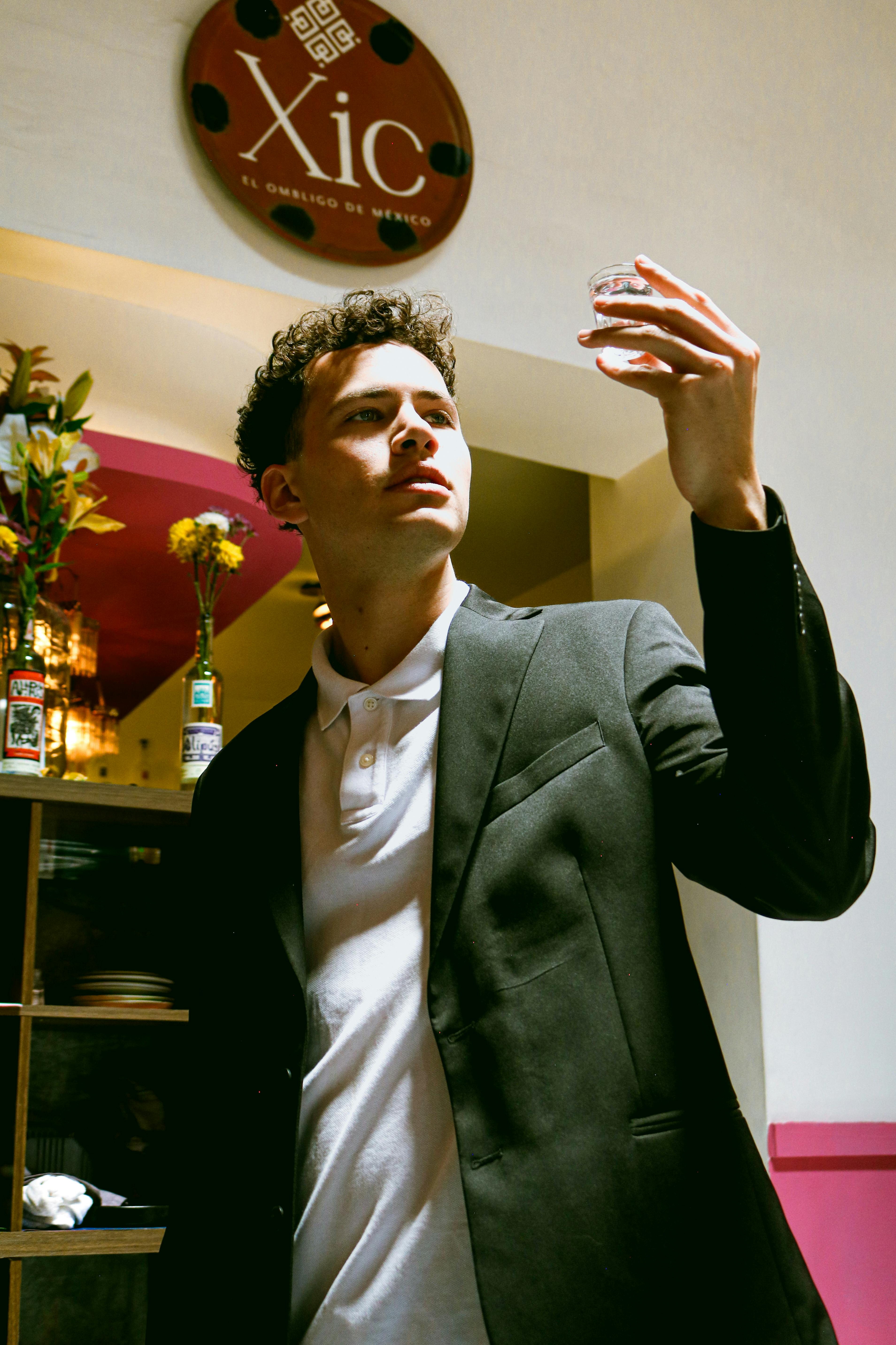 Man in suit holds a small glass in a brightly lit Mexican restaurant setting.