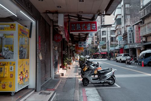 Free City street with parked scooters and vibrant storefronts in Asia, showcasing urban life. Stock Photo