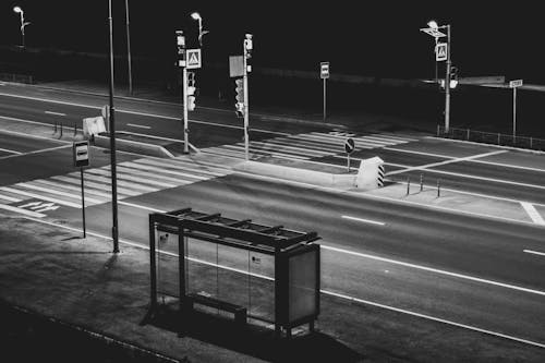 Grayscale Photography of Waiting Shed Near Open Road at Night