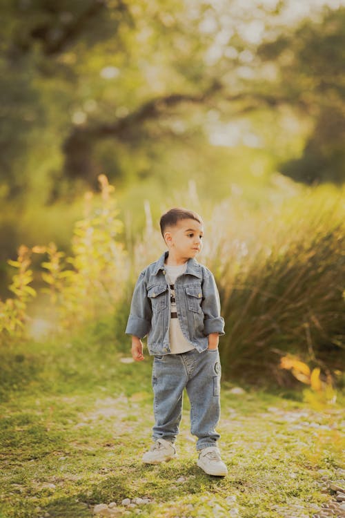 A young boy standing in the grass with his hands in his pockets