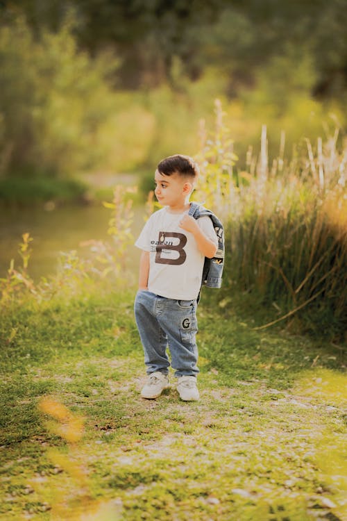 A young boy standing in the grass with a backpack