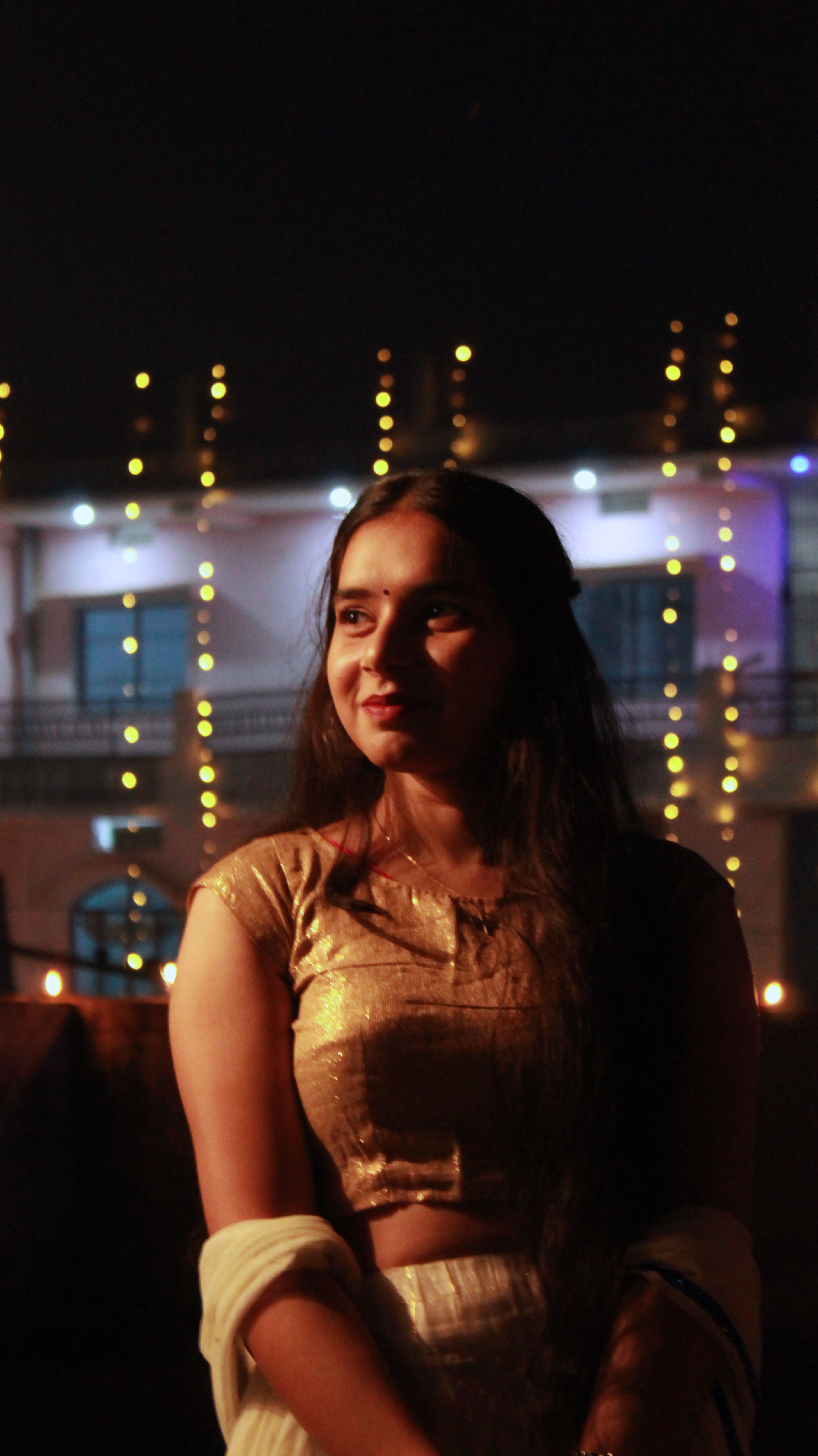 Beautiful portrait of a woman in traditional attire, surrounded by warm lights at night.