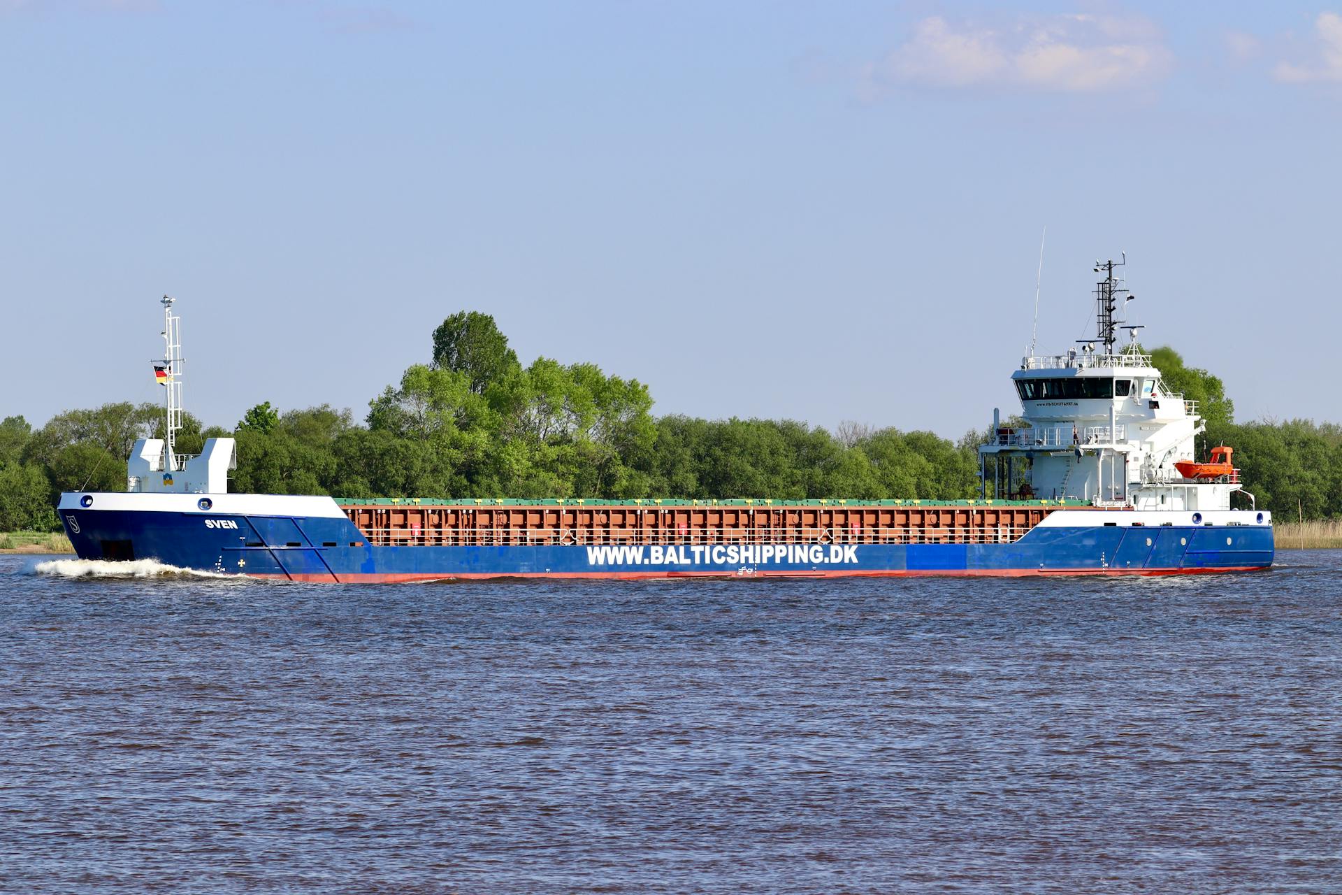 A blue cargo ship sails near a green coastline under a clear sky. Ideal for logistics themes.