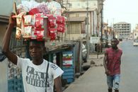 Young man balancing a tray of snacks on his head, walking down a street in Freetown, Sierra Leone.