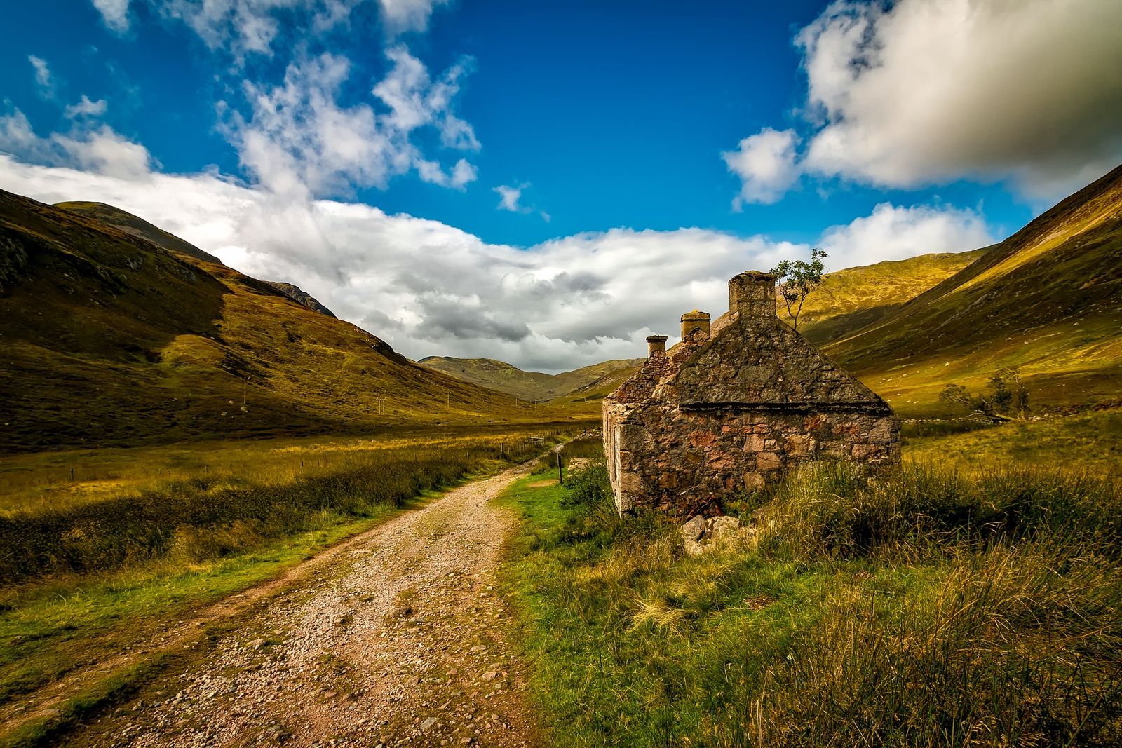 Rustic stone cottage along a dirt road amidst green hills