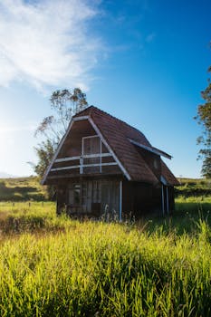 一座迷人的乡村小屋，坐落在郁郁葱葱的绿色田野之中，头顶是蔚蓝的天空