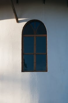 经典的拱形窗户在极简主义白色墙壁上投下柔和的阴影