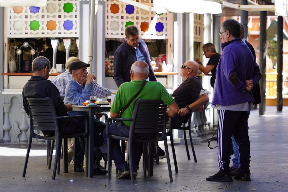 Grupo de hombres ancianos socializando en una cafetería al aire libre, disfrutando de bebidas y conversación.