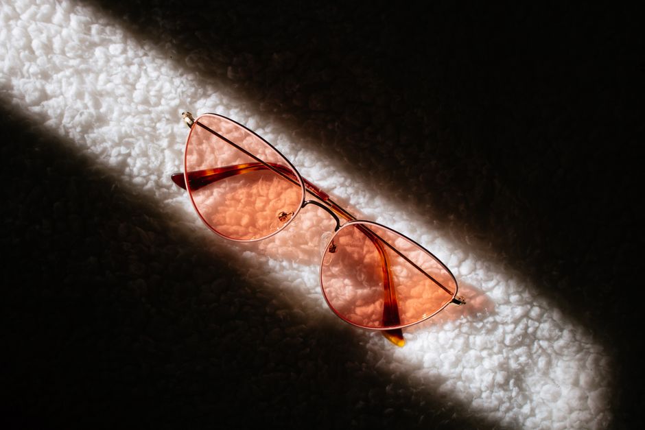 Aviator sunglasses with pink lenses placed under dramatic sunlight, casting intriguing shadows.