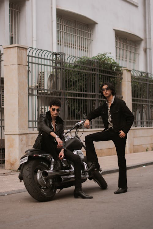 Two men in black suits and sunglasses are standing next to a motorcycle