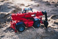 特写镜头捕捉了沙滩上红色玩具挖掘机的细节与色彩对比