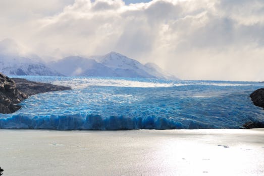 Dramatic view of a glacier with snowy mountains under cloudy skies.