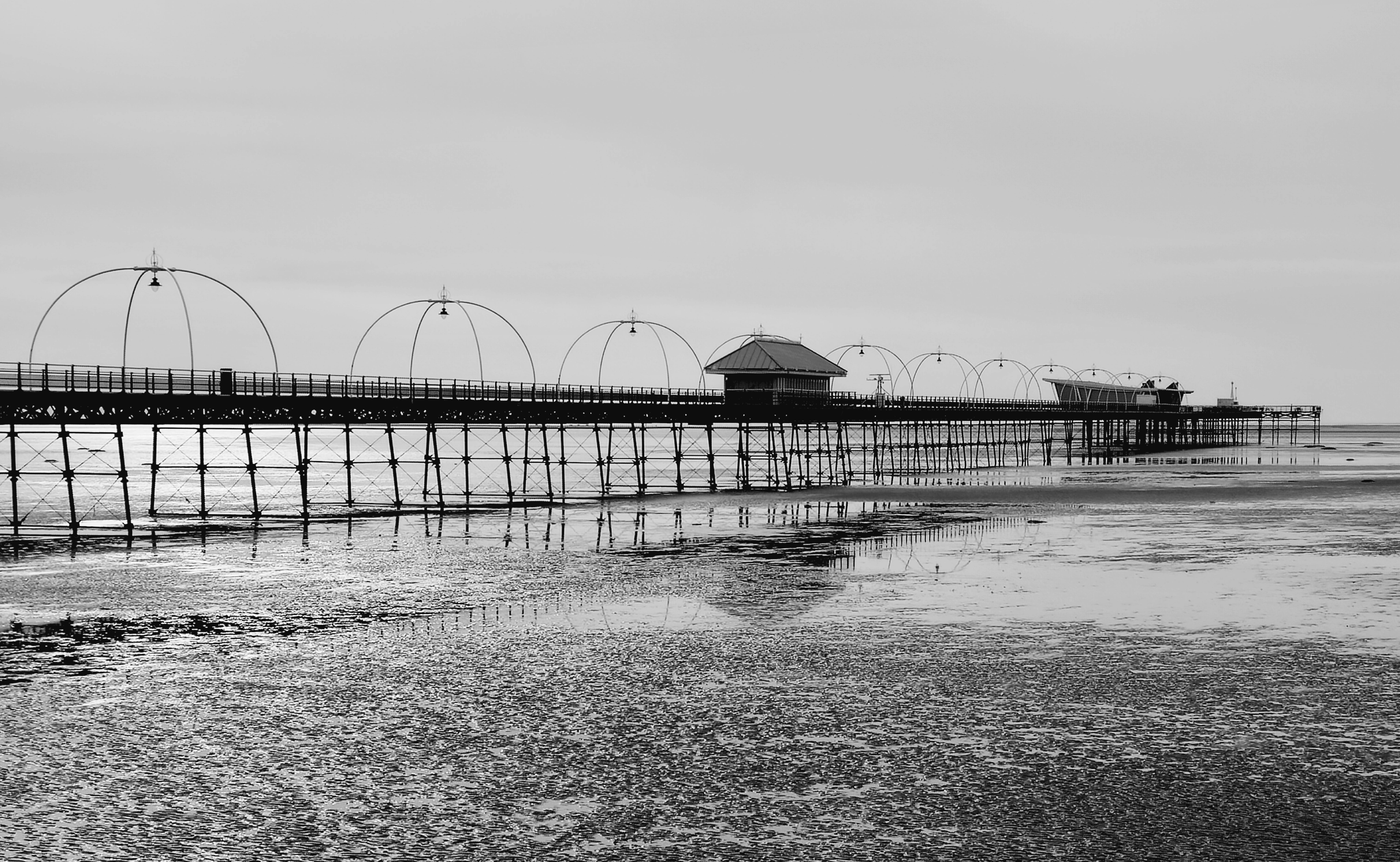 Black and white photo of Southport Pier reflecting on the sea at low tide.