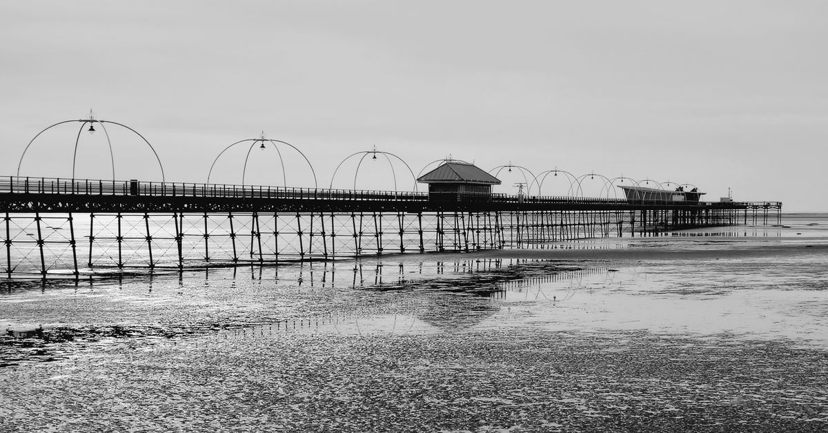 Black and white photo of Southport Pier reflecting on the sea at low tide.