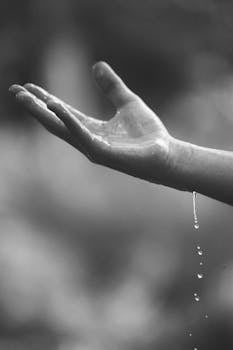 A close-up of a hand with water droplets, captured in a dramatic black and white style.