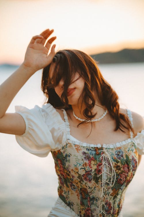 A woman in a floral dress is posing near the water