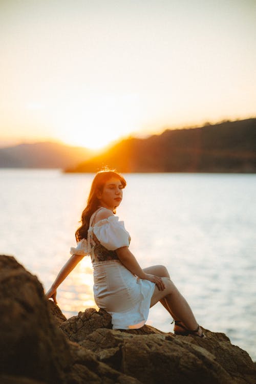 A woman sitting on a rock at sunset