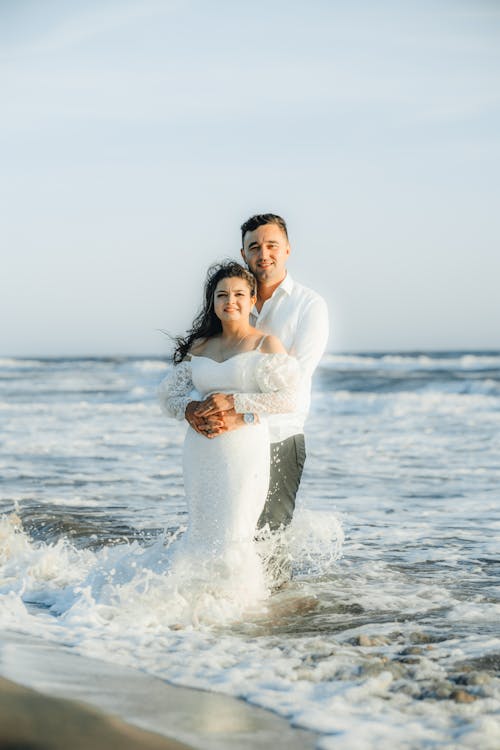 A bride and groom are standing in the ocean