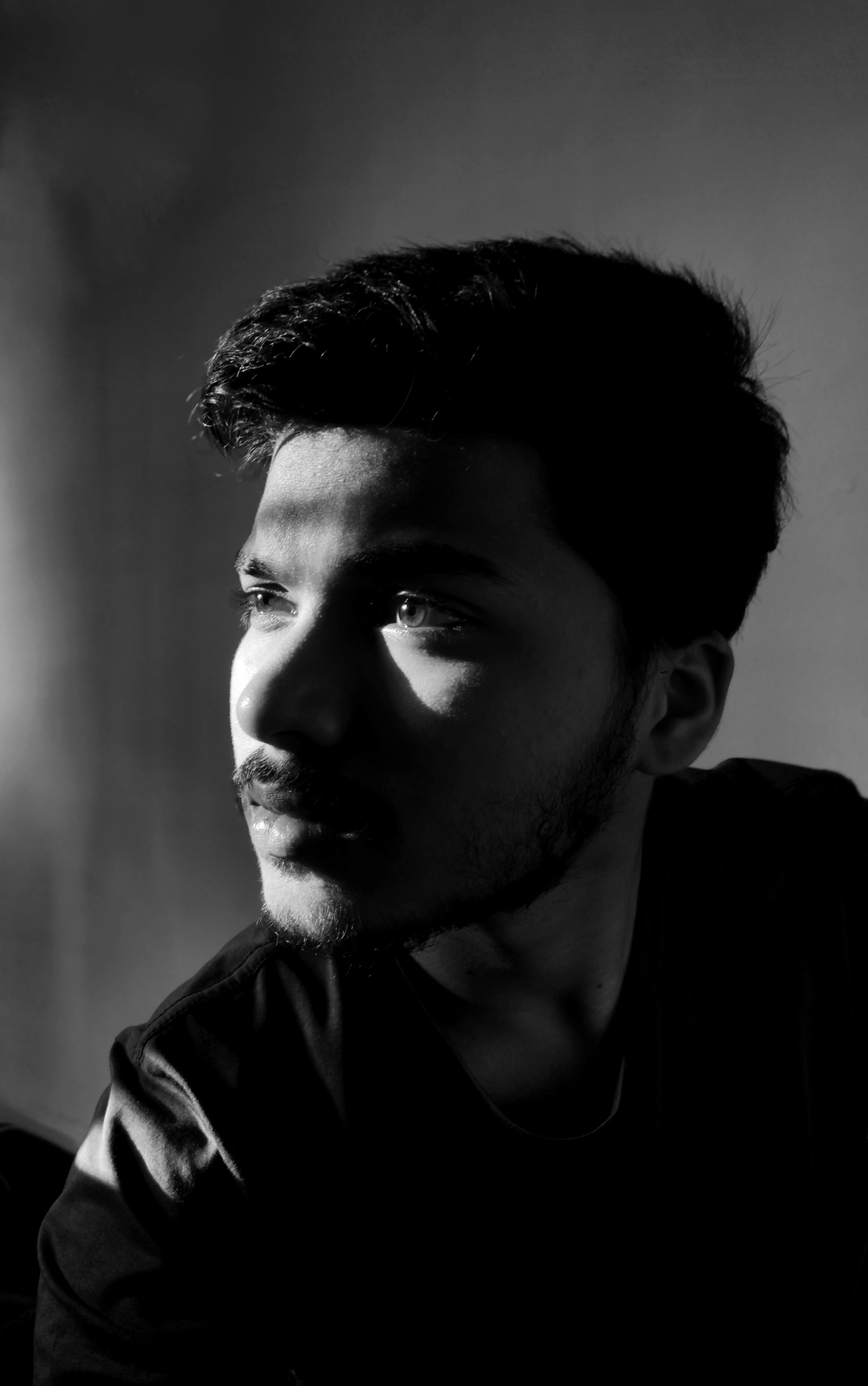 Dramatic black and white portrait of a young man with beard, gazing thoughtfully.