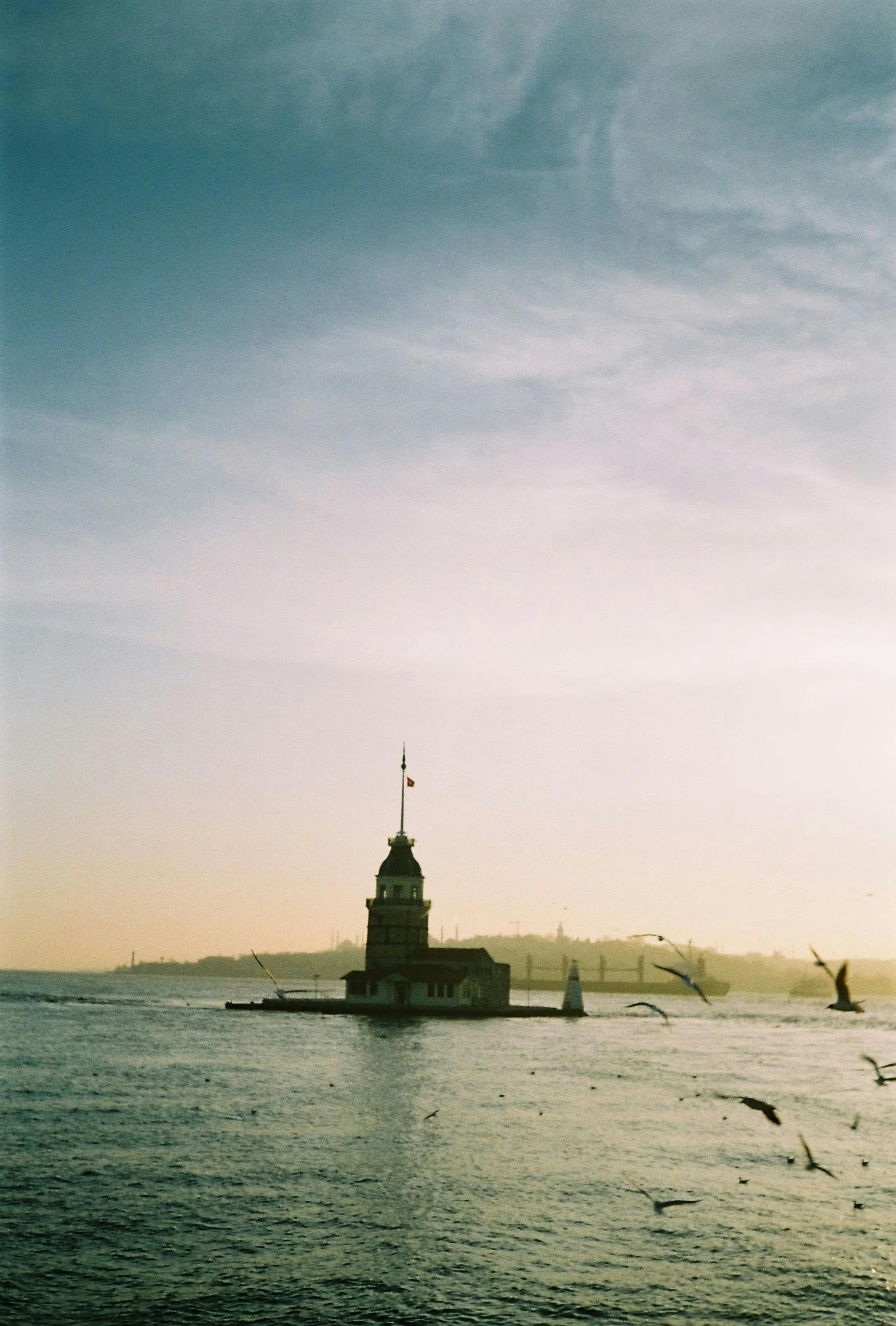 A serene view of Istanbul's Maiden's Tower during sunset, surrounded by the calm sea and flying birds.