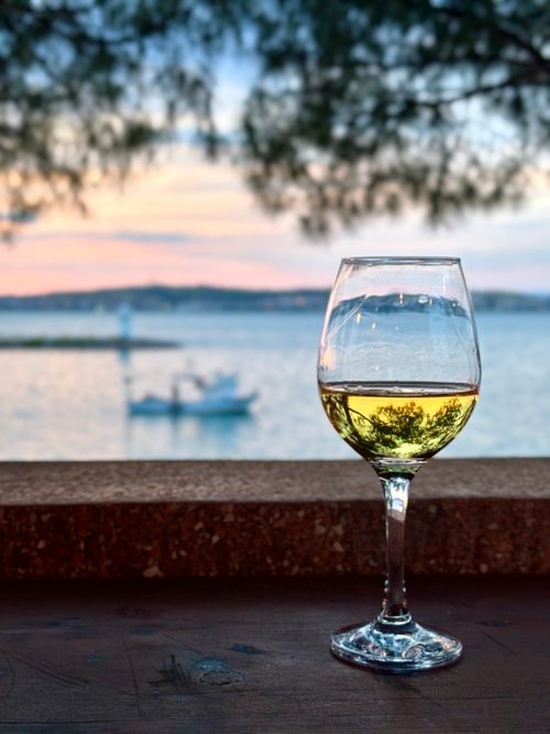 Free A tranquil seaside sunset featuring a glass of white wine with blurred background of a boat. Stock Photo