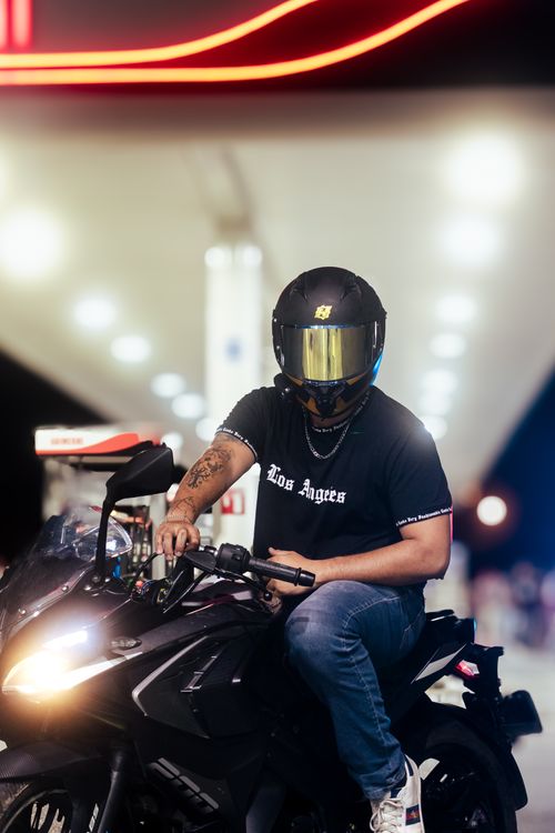 Free A man in a helmet sits on a motorcycle at a gas station, illuminated by night lights. Stock Photo