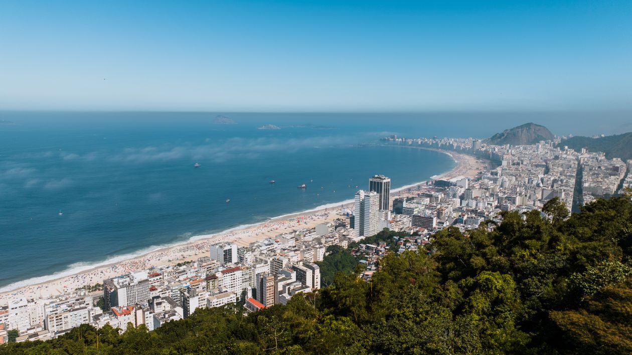Aerial view of Copacabana Beach in Rio de Janeiro with the shoreline, ocean horizon, and dense urban waterfront under bright daylight.