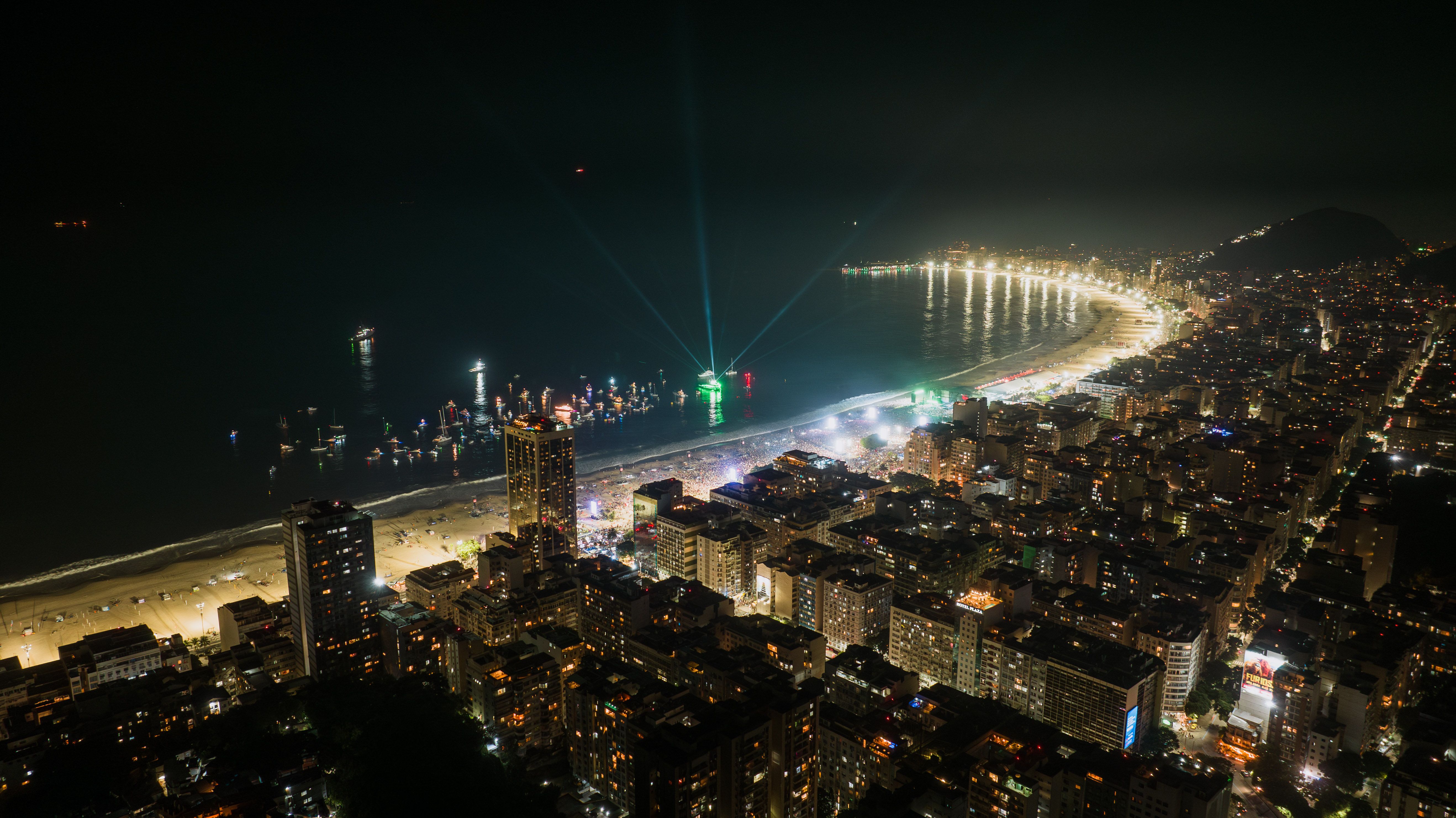Stunning aerial view of Rio de Janeiro's coastline at night, with illuminated cityscape and beach lights.