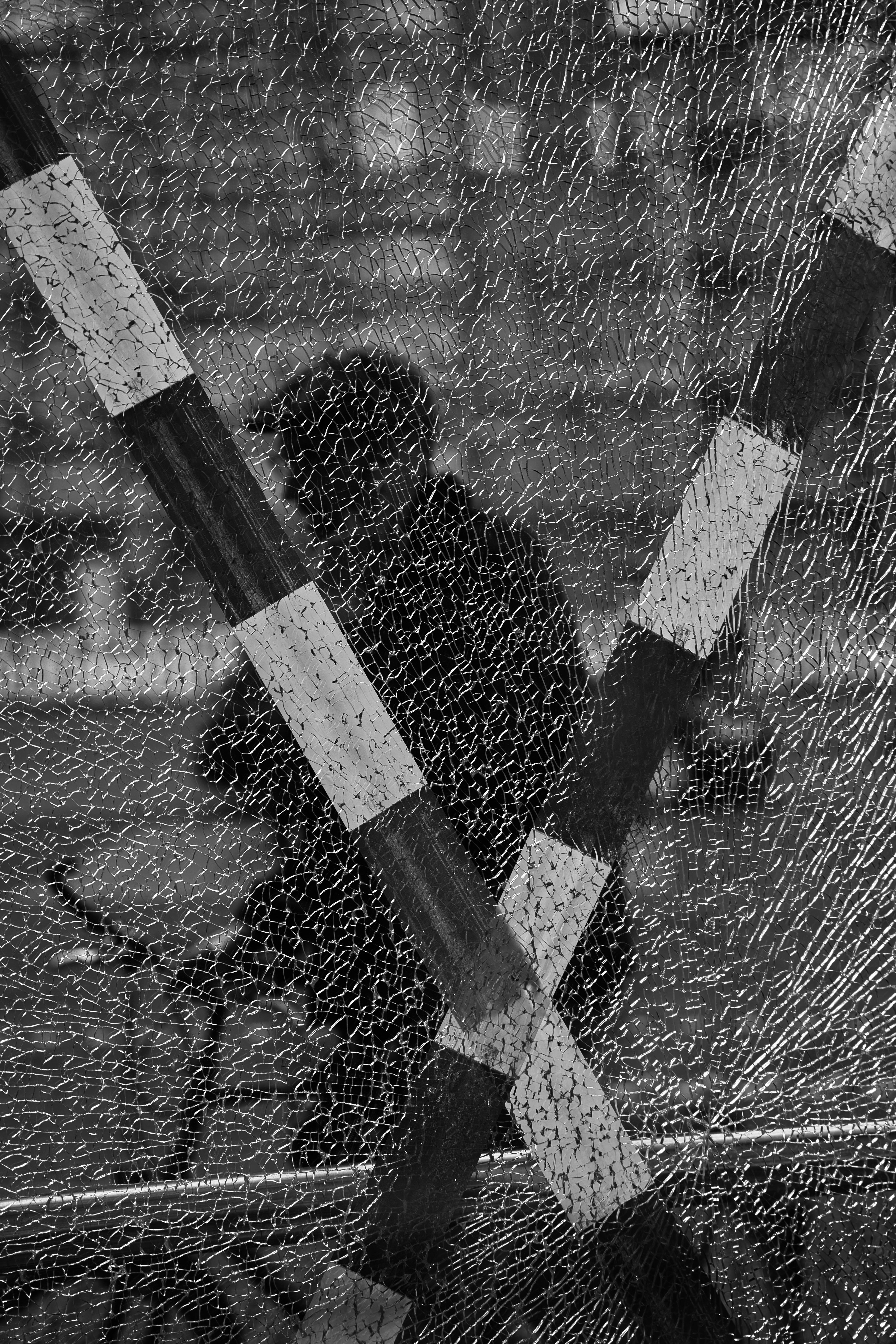 Black and white silhouette seen through shattered glass with striped bars.