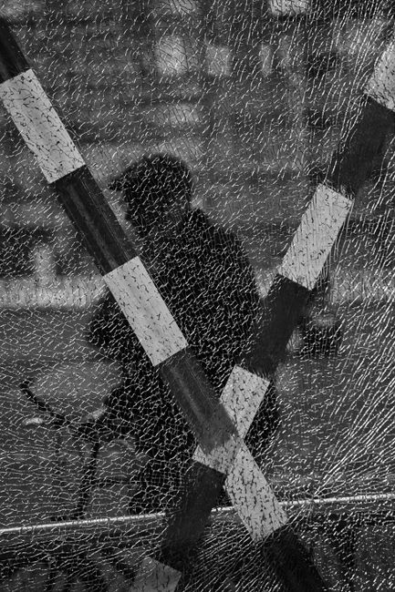 Black and white silhouette seen through shattered glass with striped bars.