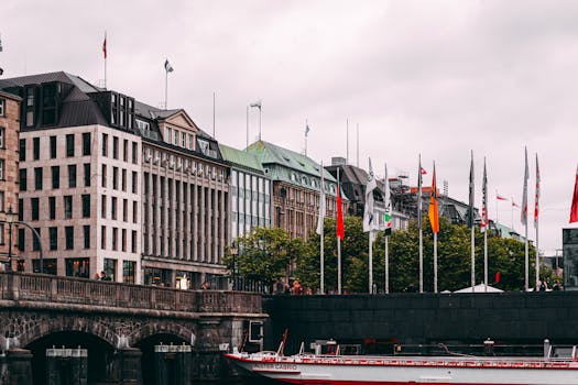 汉堡的城市风光中，多云天空下，建筑物和河流上悬挂着众多旗帜