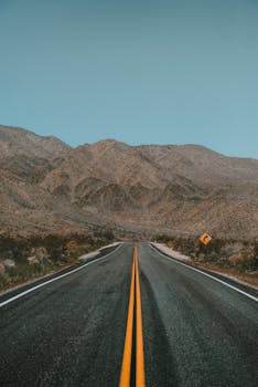 在晴朗的天空下，空旷的沙漠公路延伸向崎岖的山区