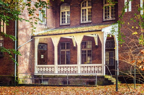 Free Beautiful view of a historic brick house with an inviting wooden porch in autumn. Stock Photo