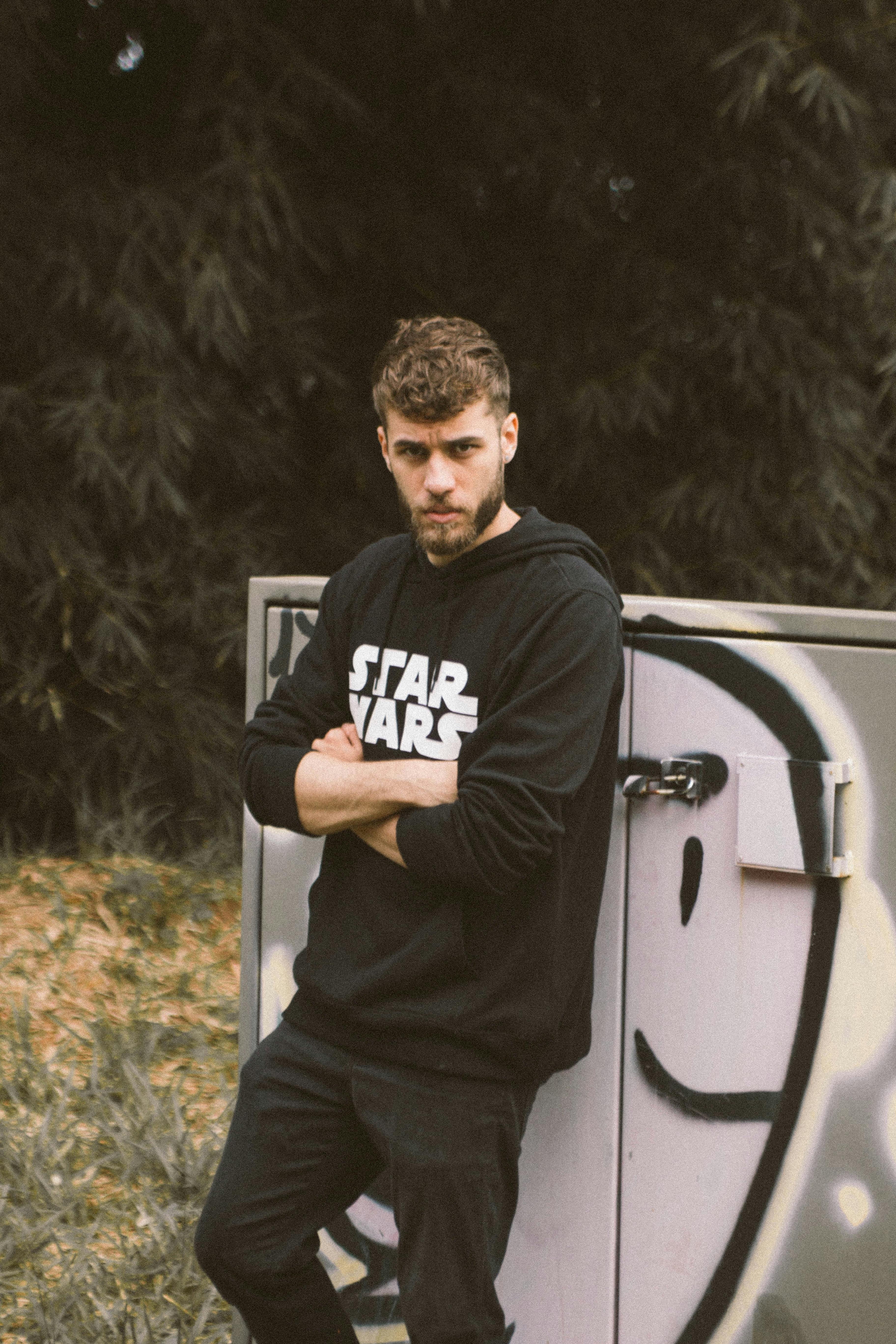 一位穿着星球大战连帽衫的年轻人在户外涂鸦前严肃地摆姿势