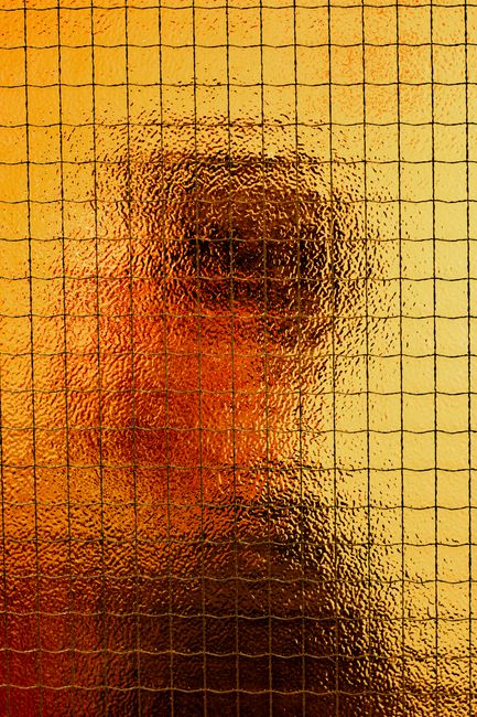 Blurred silhouette of a person through textured orange glass, creating an abstract artistic effect.