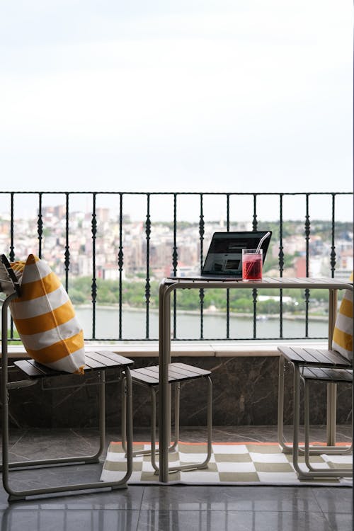 A laptop sits on a table on a balcony overlooking a city