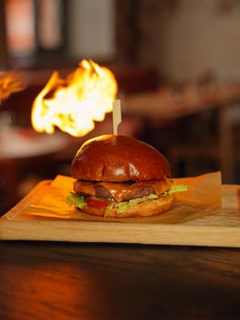 Tasty gourmet burger served on a wooden tray with a dramatic flame in a restaurant setting.