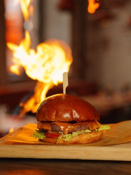Juicy gourmet burger on wooden tray with fiery background in a restaurant.