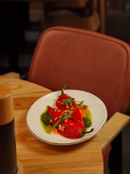 Plate of roasted red peppers garnished with herbs, served in a stylish restaurant setting.