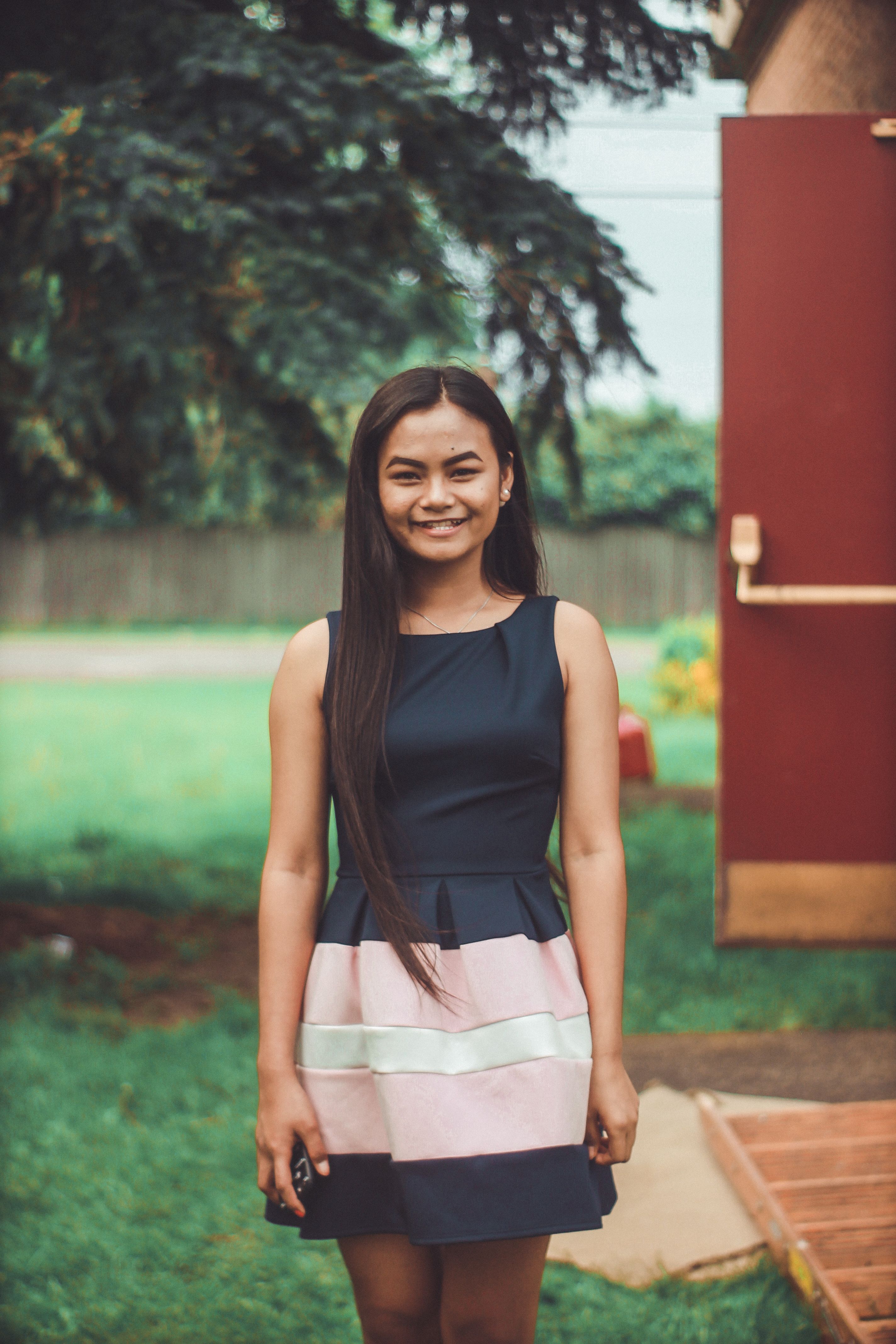 Outdoor portrait of a smiling young woman wearing a trendy dress, amidst a lush green garden.