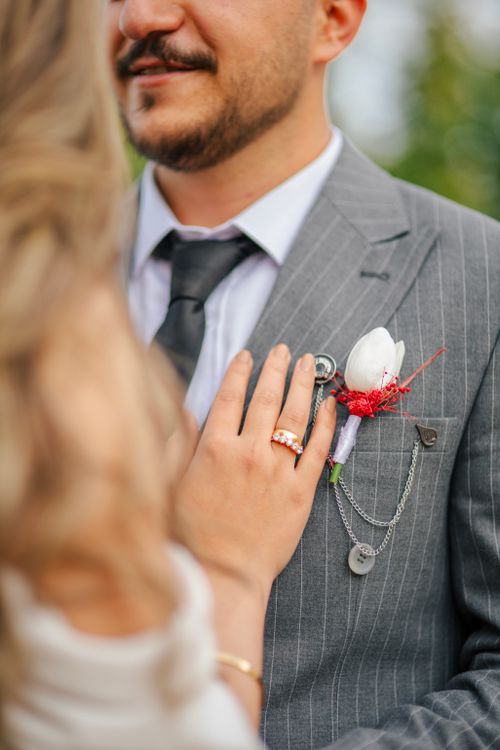 Free Intimate shot of bride's hand on groom's suit with boutonniere, capturing wedding elegance. Stock Photo