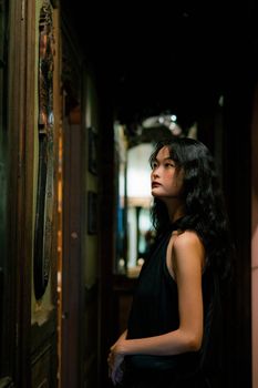 Elegant woman in black dress standing in a dimly lit hallway, showcasing stylish fashion and contemplative mood.