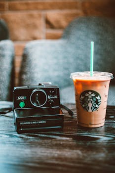 木桌上摆着一台经典的宝丽来相机，旁边放着一杯清爽的冰咖啡